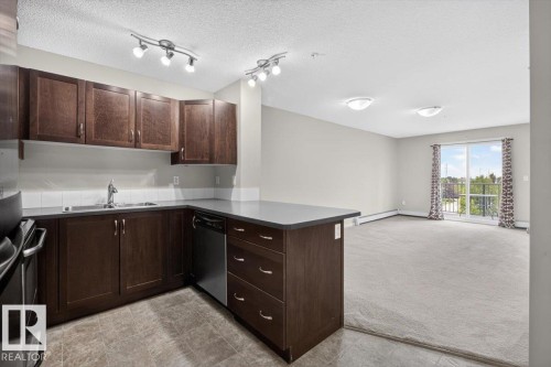 Open-concept living space with a kitchen featuring dark wood cabinetry, stainless steel appliances, and a gray countertop - #316 392 Silver Berry Rd Nw, Edmonton, AB - Indoor Photo Showing Kitchen With Double Sink