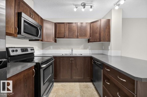 U-shaped kitchen featuring dark wood cabinetry, light grey countertops, a stainless steel microwave, a black electric range, and a black dishwasher - #316 392 Silver Berry Rd Nw, Edmonton, AB - Indoor Photo Showing Kitchen With Double Sink