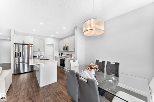 Open-concept kitchen and dining area featuring wood-finish flooring, white cabinetry, stainless steel appliances, and an island with a sink - 2628 Donaghey Crescent Sw, Edmonton, AB 