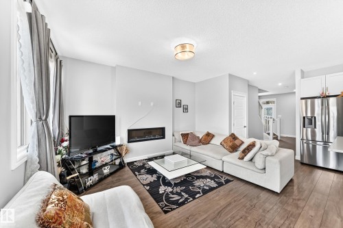 Integrated living area featuring wood-finish flooring, a linear electric fireplace, and a contemporary ceiling light fixture - 2628 Donaghey Crescent Sw, Edmonton, AB 