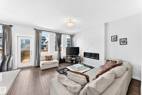 Open-concept living area with wood-finish flooring, multiple windows, a glass-paneled exterior door, and an integrated linear fireplace - 2628 Donaghey Crescent Sw, Edmonton, AB 