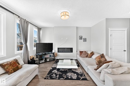 Wood-finish flooring throughout, multiple windows with white trim, built-in electric fireplace, recessed ceiling lighting, and a white paneled interior door - 2628 Donaghey Crescent Sw, Edmonton, AB 