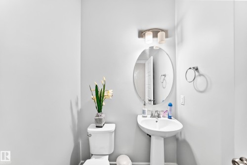 Pedestal sink with chrome faucet, oval mirror, and wall-mounted light fixture - 2628 Donaghey Crescent Sw, Edmonton, AB 