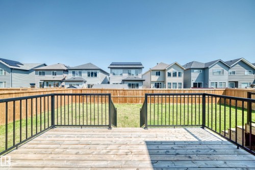 Wood-finish deck with black metal railing, overlooking a fenced backyard with a grass lawn - 2628 Donaghey Crescent Sw, Edmonton, AB 