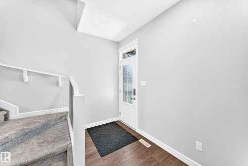 Entryway featuring wood-finish flooring, a white paneled door with textured glass, and a carpeted staircase with white railings - 2628 Donaghey Crescent Sw, Edmonton, AB 