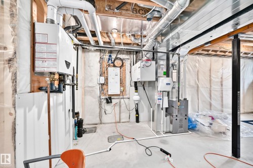 Unfinished basement space featuring exposed ductwork, a tankless water heater, and a furnace system - 2628 Donaghey Crescent Sw, Edmonton, AB 