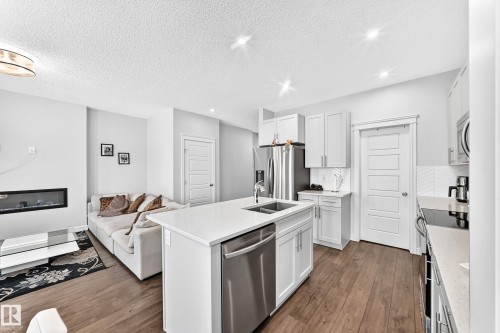 Open-concept living area with wood-finish flooring, a linear fireplace, and a kitchen island featuring a stainless steel double sink - 2628 Donaghey Crescent Sw, Edmonton, AB 