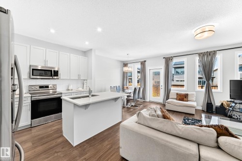 Kitchen featuring stainless steel appliances, white cabinetry, a kitchen island with sink, and wood-finish flooring - 2628 Donaghey Crescent Sw, Edmonton, AB 