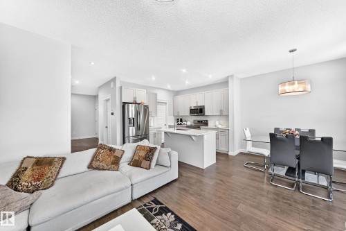Spacious open-concept living area featuring wood-finish flooring, recessed lighting, and a kitchen island with seating - 2628 Donaghey Crescent Sw, Edmonton, AB 