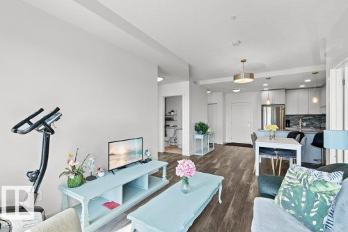 Open-concept living space featuring wood-finish flooring throughout, a modern kitchen with stainless steel appliances, a breakfast bar, and pendant lighting - 1316 Windermere Way Sw, Edmonton, AB 