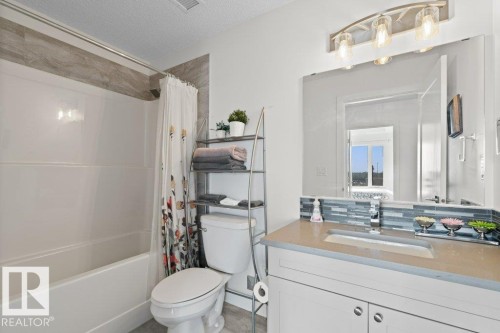 Bathroom featuring a combined tub and shower, a single vanity with a solid surface countertop, an integrated sink, and an extensive wall mirror - 1316 Windermere Way Sw, Edmonton, AB 