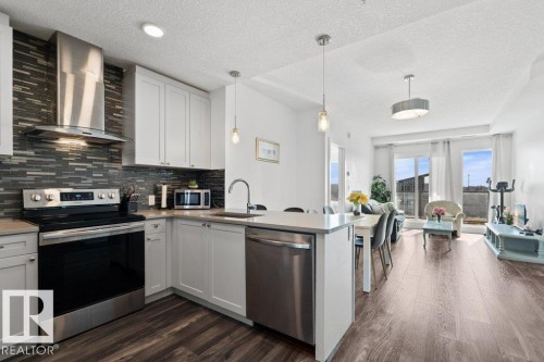 Contemporary kitchen featuring white cabinetry, stainless steel appliances, a tile backsplash, and a breakfast bar - 1316 Windermere Way Sw, Edmonton, AB 