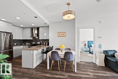 Kitchen featuring white cabinetry, stainless steel appliances, dark tile backsplash, and an island with counter seating - 1316 Windermere Way Sw, Edmonton, AB 