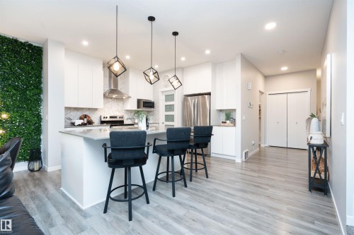 Open-concept kitchen with light wood-finish flooring, white cabinetry, and stainless steel appliances - 9232 224 St Nw Nw, Edmonton, AB 