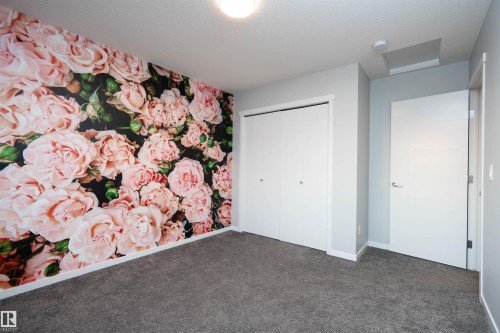 Wall featuring a floral pattern, neutral-toned carpeting, white bi-fold closet doors, and a modern single-panel interior door - 9232 224 St Nw Nw, Edmonton, AB 