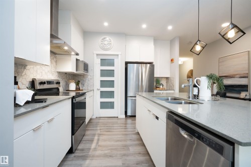 Modern kitchen featuring white cabinetry, stainless steel appliances, light-toned countertops, tile backsplash, and wood-finish flooring - 9232 224 St Nw Nw, Edmonton, AB 