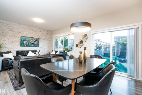 Wood-finish flooring, white brick-style accent wall, built-in fireplace, sliding glass door, and a modern circular pendant light - 9232 224 St Nw Nw, Edmonton, AB 