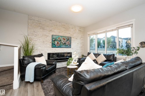 Living area featuring a stone accent wall, linear electric fireplace, and large windows - 9232 224 St Nw Nw, Edmonton, AB 