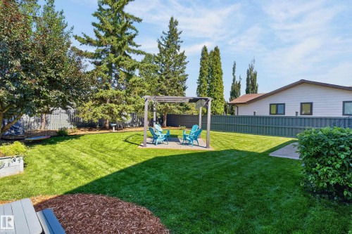 Expansive backyard featuring a lush lawn, mature trees, a privacy fence, and a patio with a pergola - 18316 71 Avenue Nw, Edmonton, AB 
