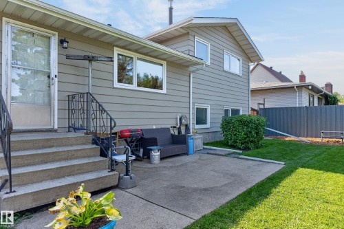 Concrete patio with a manicured lawn, established shrubbery, and a corrugated privacy fence - 18316 71 Avenue Nw, Edmonton, AB 