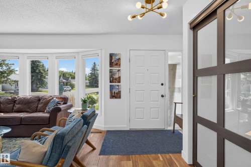 Hardwood flooring, bay windows, white paneled entry door, contemporary ceiling light fixture, and a sliding door with frosted glass panels - 18316 71 Avenue Nw, Edmonton, AB 