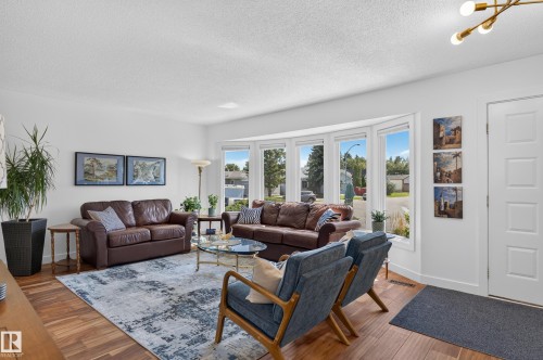 Bright living area featuring wood-finish flooring, a multi-pane bay window, white walls, and a contemporary ceiling light fixture - 18316 71 Avenue Nw, Edmonton, AB 