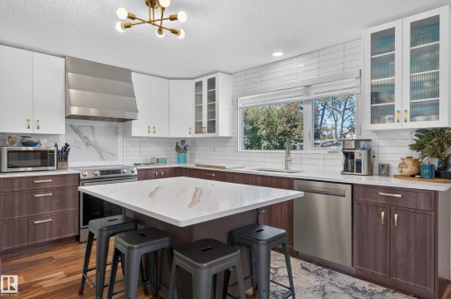 Modern kitchen featuring white upper cabinetry, rich wood-finish lower cabinetry, and a central island with a light-toned countertop - 18316 71 Avenue Nw, Edmonton, AB 