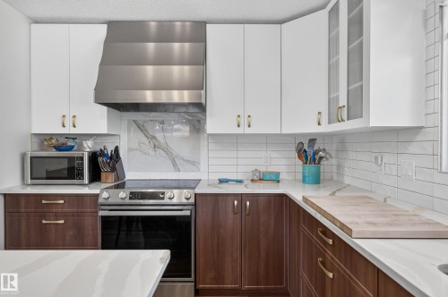 Two-tone cabinetry, stainless steel range with overhead hood, white subway tile backsplash, and light-toned countertops - 18316 71 Avenue Nw, Edmonton, AB 