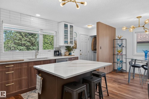 Kitchen featuring a large window, white subway tile backsplash, wood-finish cabinetry with gold-toned hardware, center island with a light-toned countertop, and wood-finish flooring - 18316 71 Avenue Nw, Edmonton, AB 