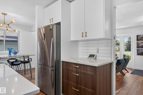 Stainless steel refrigerator, white upper cabinetry, white subway tile backsplash, wood-finish lower cabinetry, and light-colored countertops - 18316 71 Avenue Nw, Edmonton, AB 