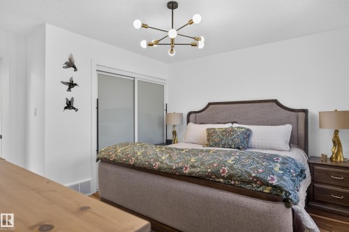 Upholstered bed frame with a sculpted headboard, wood-finish flooring, and a contemporary ceiling light fixture - 18316 71 Avenue Nw, Edmonton, AB 