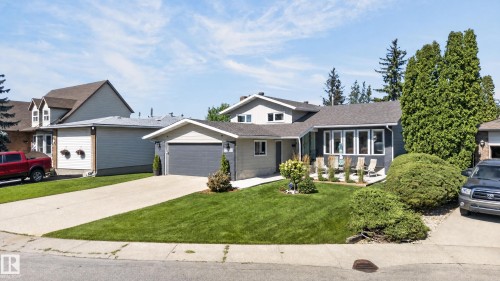 Exterior featuring a dark gray garage door, bay window, concrete driveway, and mature landscaping - 18316 71 Avenue Nw, Edmonton, AB 