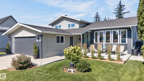 Contemporary exterior featuring siding and painted brick accents, an attached garage with a dark gray door, a paved driveway, and a front patio with perimeter landscaping - 18316 71 Avenue Nw, Edmonton, AB 