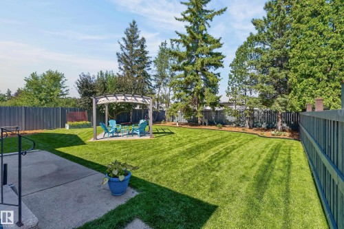 Expansive backyard featuring a manicured lawn, a built-in pergola, mature trees, and a concrete patio - 18316 71 Avenue Nw, Edmonton, AB 