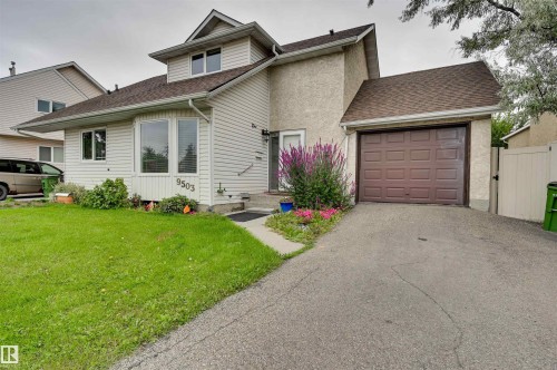 Siding exterior with a bay window, attached garage, paved driveway, and established landscaping - 9503 180A Street Nw, Edmonton, AB 