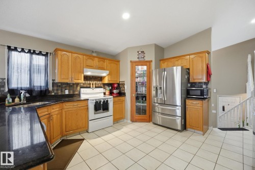 Wood-finish cabinetry paired with dark countertops, a tile backsplash, and white tile flooring - 5132 157 Avenue Nw, Edmonton, AB 
