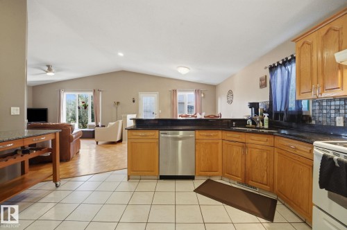 Kitchen featuring wood cabinetry, dark countertops, tile flooring, and a stainless steel dishwasher - 5132 157 Avenue Nw, Edmonton, AB 