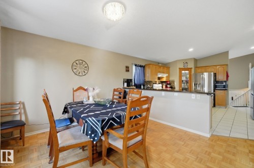 Open-concept kitchen with wood cabinetry, stainless steel appliances, and a breakfast bar, complemented by wood-finish flooring - 5132 157 Avenue Nw, Edmonton, AB 