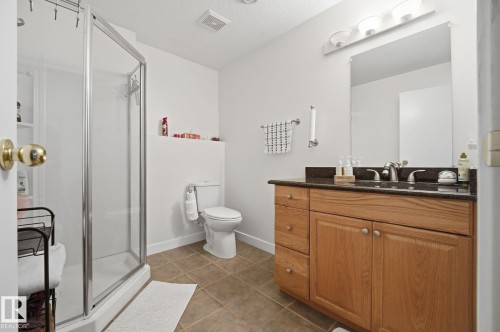 Bathroom featuring a glass-enclosed shower, wood-finish vanity with drawer storage, dark countertop, and tiled flooring - 5132 157 Avenue Nw, Edmonton, AB 