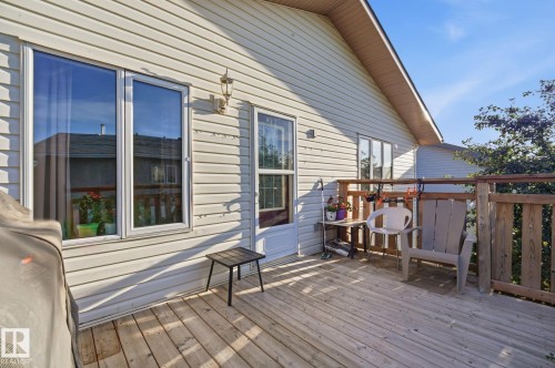 Wood-finish deck with a wood railing, leading to a white vinyl-sided exterior - 5132 157 Avenue Nw, Edmonton, AB 