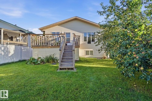 Expansive backyard featuring a manicured lawn, a large wood deck with stairs, multiple windows providing natural light, and mature trees - 5132 157 Avenue Nw, Edmonton, AB 