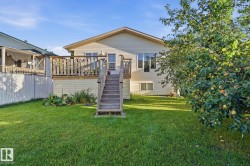 Expansive backyard featuring a manicured lawn, a large wood deck with stairs, multiple windows providing natural light, and mature trees - 