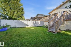 Expansive backyard featuring a manicured lawn, a chain-link fence, and a multi-level wood deck with stairs - 