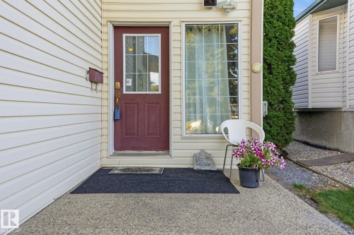 Cream-colored siding exterior with a red front door featuring a divided light window - 5132 157 Avenue Nw, Edmonton, AB 