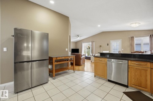 Open-concept kitchen featuring tile flooring, wood cabinetry, stainless steel dishwasher, and a stone-finish countertop - 5132 157 Avenue Nw, Edmonton, AB 