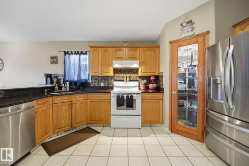 Kitchen featuring wood cabinetry, dark countertops, tiled backsplash, and stainless steel appliances - 5132 157 Avenue Nw, Edmonton, AB 