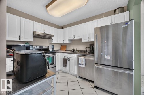 Kitchen featuring white cabinetry, stainless steel appliances, a range hood, and tile flooring - #1102 9916 113 St Nw, Edmonton, AB 