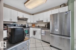 Kitchen featuring white cabinetry, stainless steel appliances, a range hood, and tile flooring - 