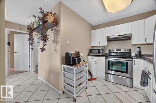 White shaker-style cabinetry, stainless steel range, stainless steel over-the-range microwave, dark countertops, and diagonal tile flooring - #1102 9916 113 St Nw, Edmonton, AB 