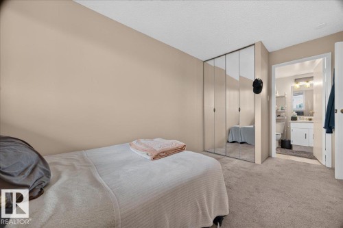 Plush carpeted flooring, neutral wall tones, mirrored closet doors, and an en-suite bathroom with a white vanity - #1102 9916 113 St Nw, Edmonton, AB 